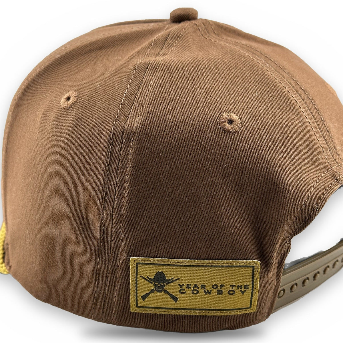 A brown canvas snapback cap shown from the back, featuring a tan rectangular patch with a black skull and crossbones logo and the text 'YEAR OF THE COWBOY'.