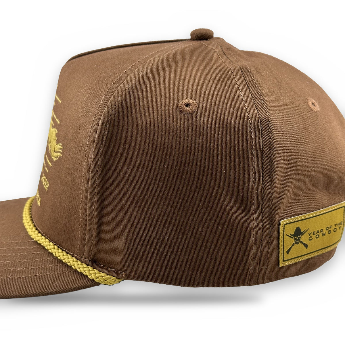 A brown cotton flat-brim cap with a yellow braided rope detail along the edge of the brim, featuring a yellow embroidered fish logo on the side and a yellow 'SILK STOCK' patch on the back.